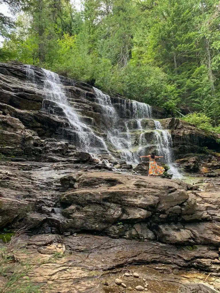 A woman in a dress poses in front of Moses Falls in Revelstoke