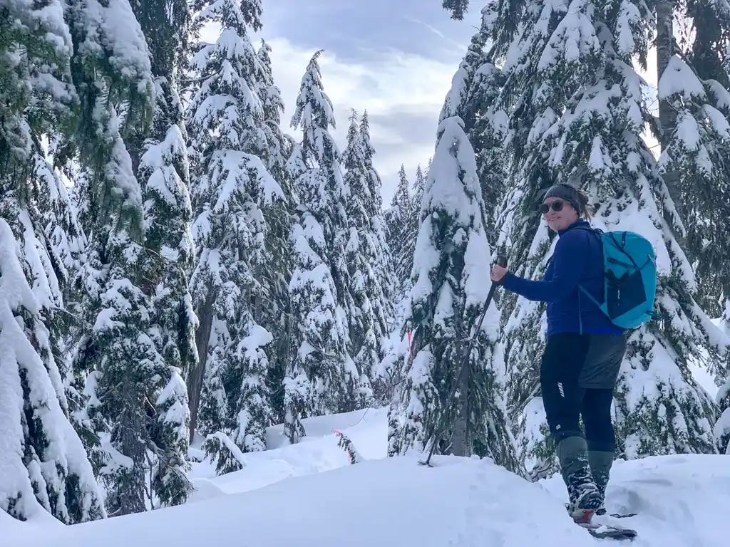 A woman wearing a down skirt snowshoes through a snowy forest