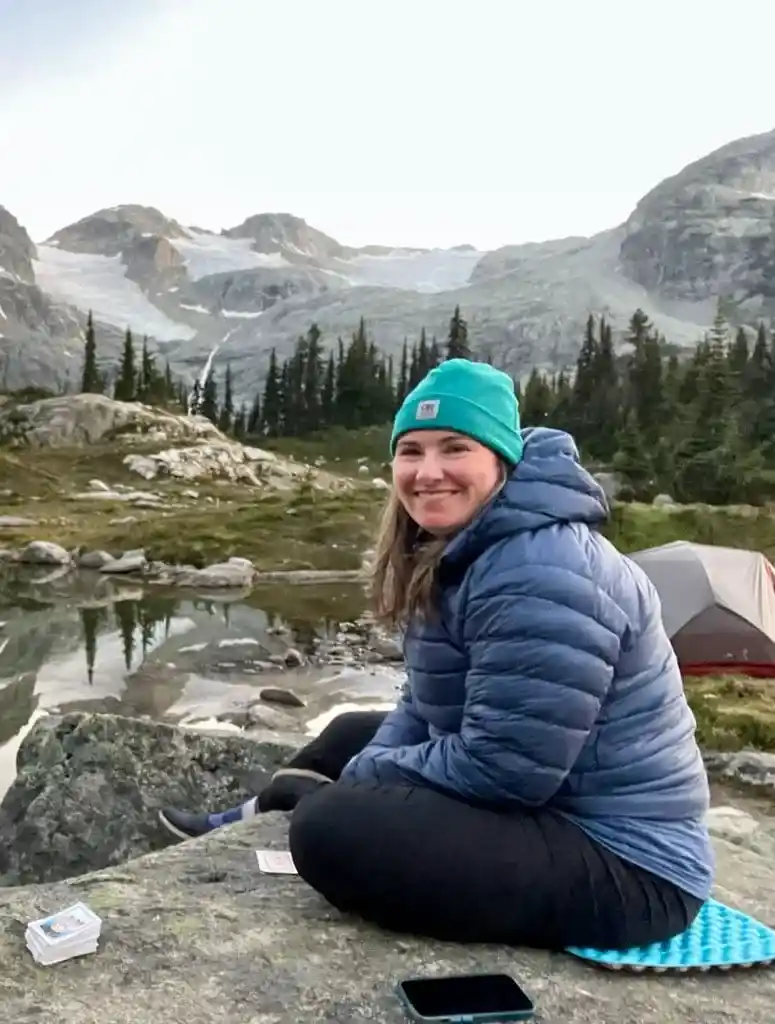 A woman wears an Arc'teryx Cerium down jacket while sitting on a rock in the mountains. 