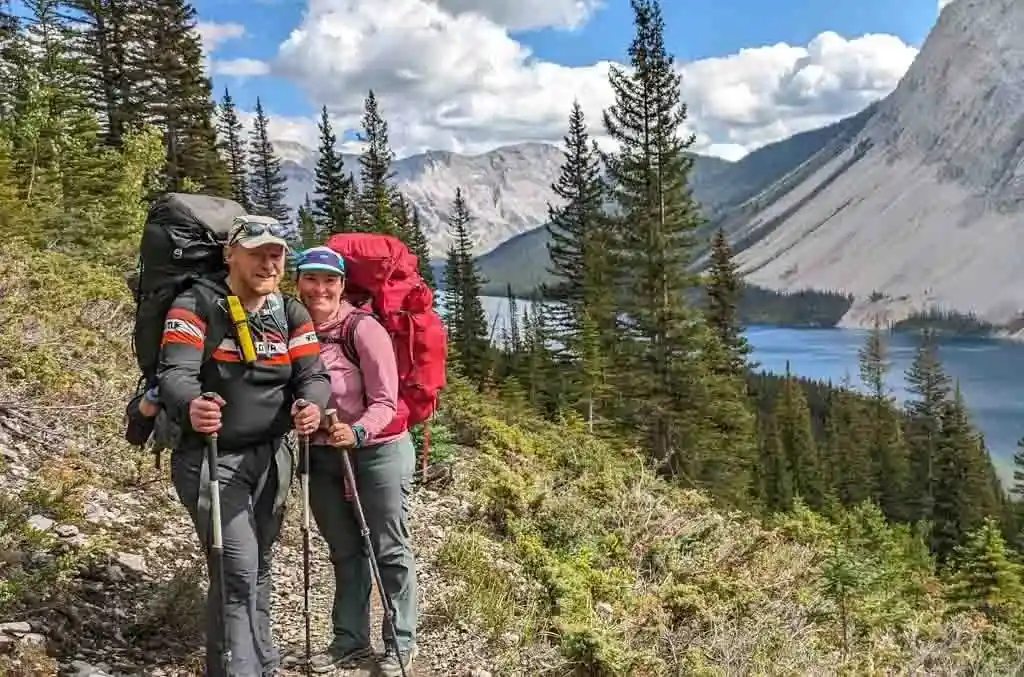 Two hikers post in the Canadian Rocky Mountains wearing big backpacking packs