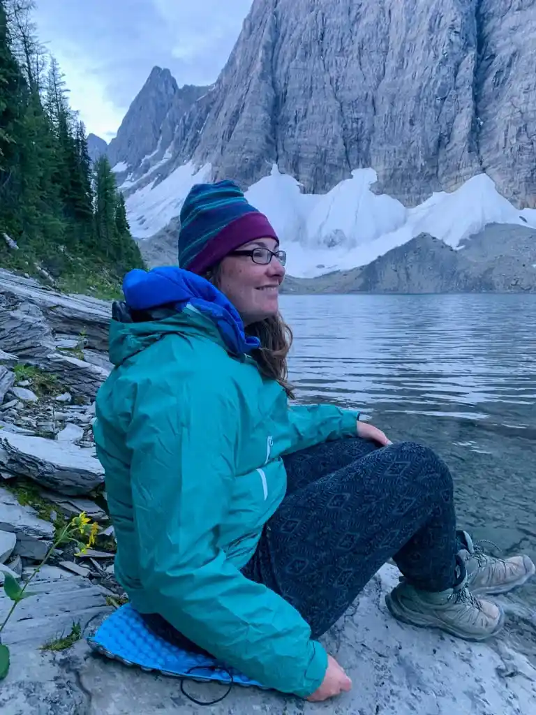 A woman wearing Merino wool base layer bottoms sits next to Floe Lake