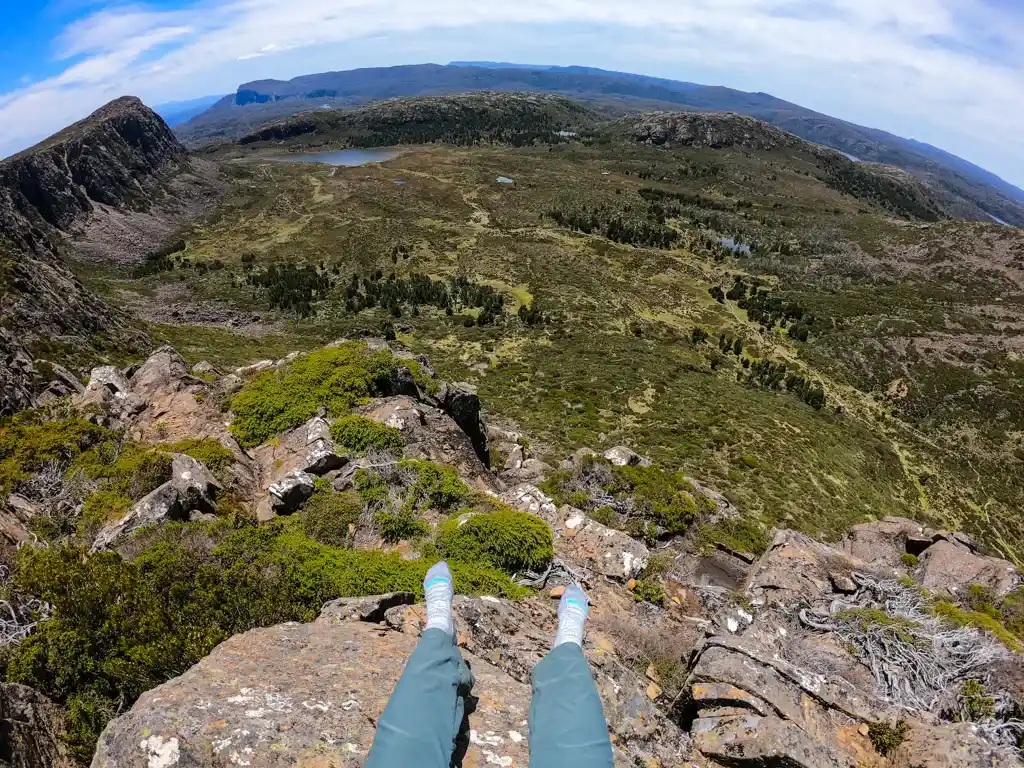 A hiker dangles their sock-clad feet off a cliff at Walls of Jerusalem National Park in Australia