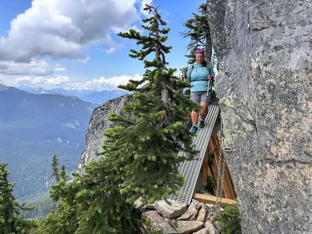 A female hiker walks down a metal ramp around a rock