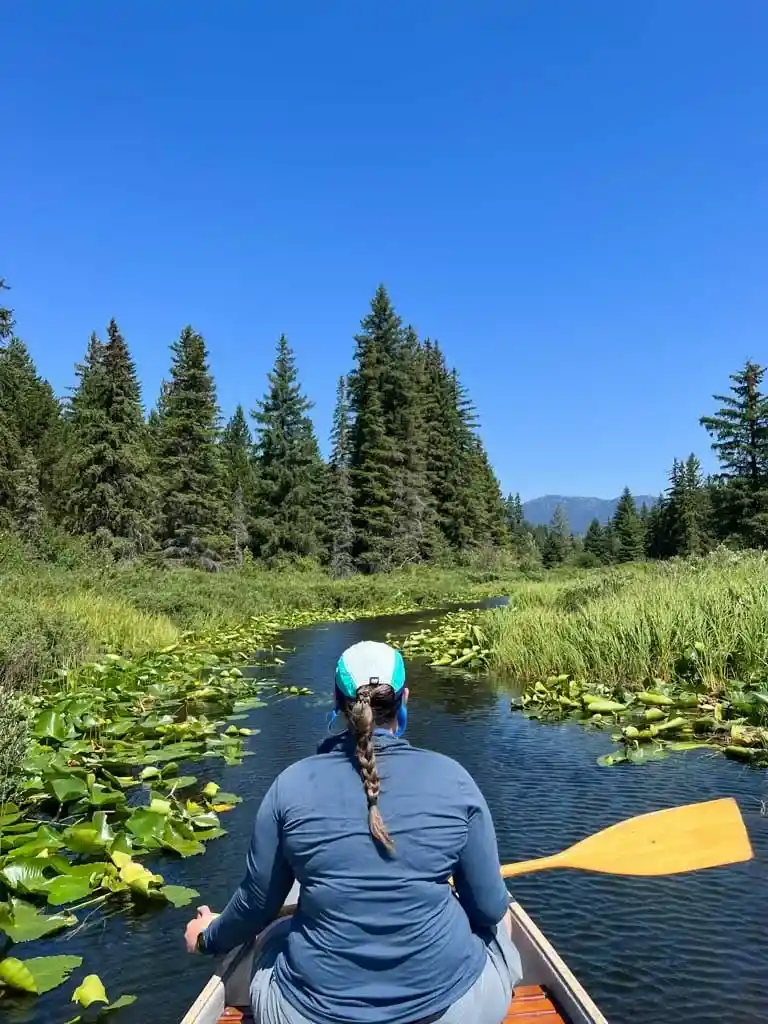 A woman paddles a canoe through a narrow stream on the River of Golden Dreams in Whistler, BC in summer.