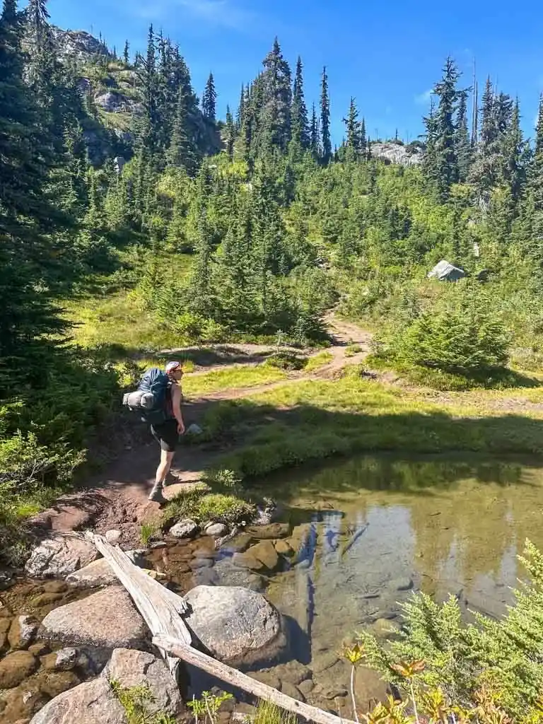 A hiker crosses a creek on an alpine trail near Pemberton