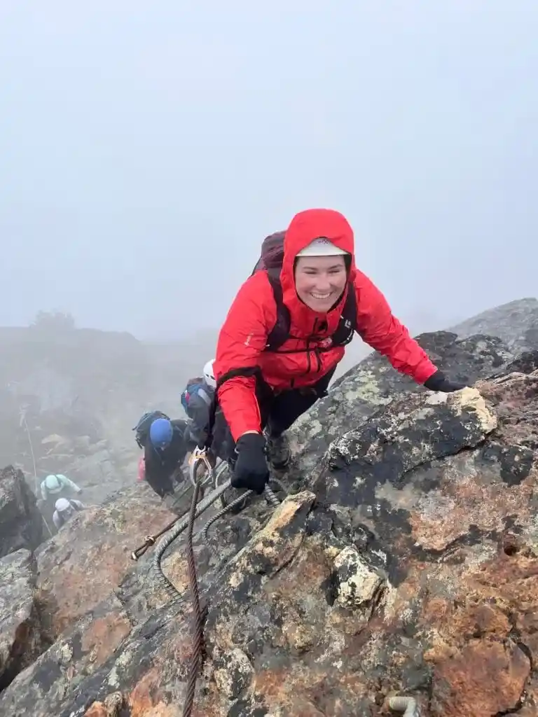 A woman smiles while holding on to meta ladder rungs on the Whistler Via Ferrata.