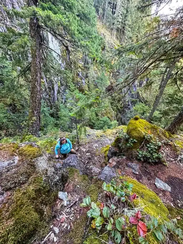 A woman climbs up a steep and scrambly trail over rock bluffs at High Falls Creek