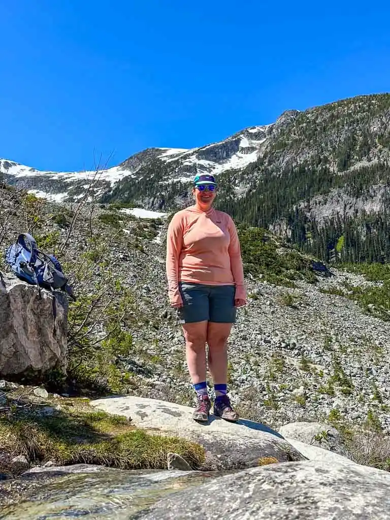A hiker poses for a photo on a rocky mountain wearing the Helly Hansen Solen Lifa Active Sun Hoodie.