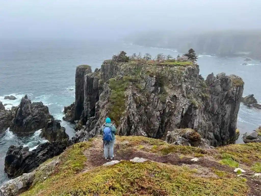 A woman in a beanie hat and warm jacket takes a photo of Puffins in Newfoundland