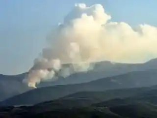 A plume of smoke rises above a forested mountain. Get tips for safe hiking in wildfire season