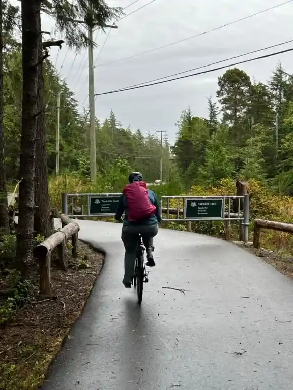A woman wearing a pink backpack bikes on the ʔapsčiik t̓a&scaron;ii bike path in Pacific Rim National Park