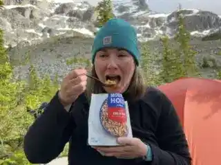 A hiker eats a Mountain House backpacking meal at a campsite. It is one of the best backpacking meals she reviewed.